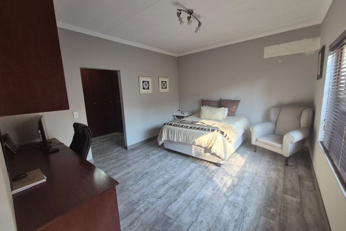 Spacious bedroom featuring laminate flooring, built-in cupboards, and venetian blinds. The room includes a dedicated workspace area and requires minor wall finishing.