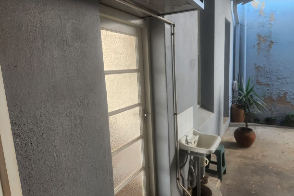 A rear exterior utility area featuring a concrete floor, an external door, and a wall-mounted utility sink with visible paint deterioration on the surrounding walls.