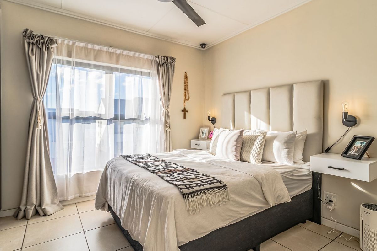 A well-maintained bedroom featuring tiled flooring, built-in cupboards, a ceiling fan, and modern floating bedside tables with integrated lighting.