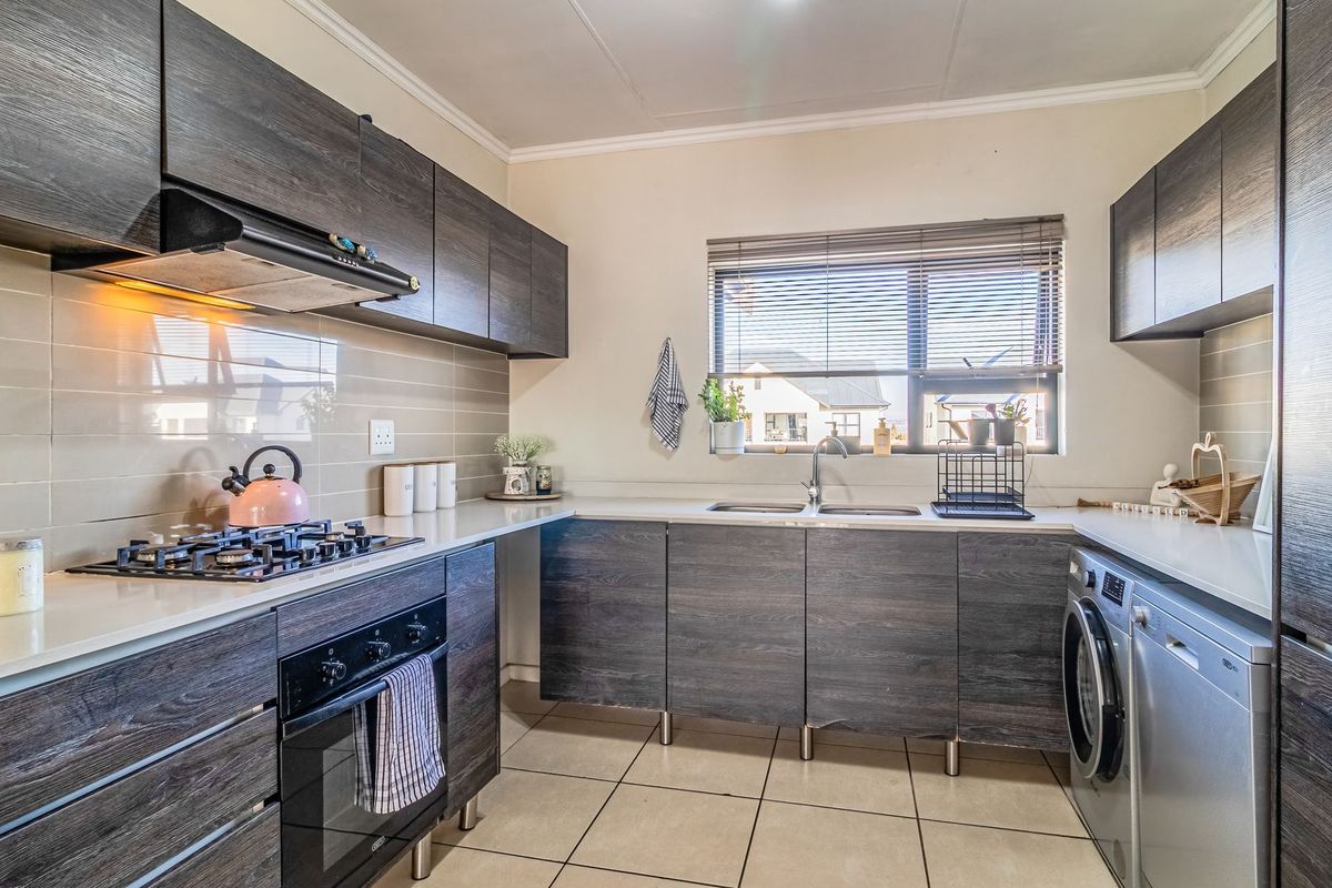 Modern kitchen featuring dark wood-grain cabinetry, stone-look countertops, gas hob, built-in oven, and integrated space for laundry appliances.