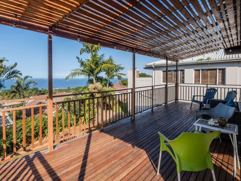Spacious elevated timber deck featuring a slatted pergola, metal balustrade, and expansive ocean views, perfect for outdoor entertaining.