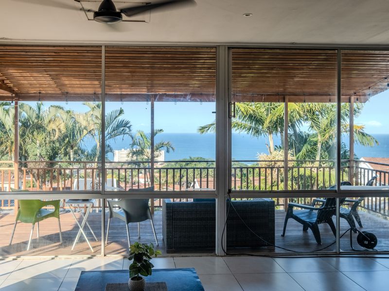 A covered balcony featuring timber decking and a pergola, offering expansive ocean views through large sliding glass doors.