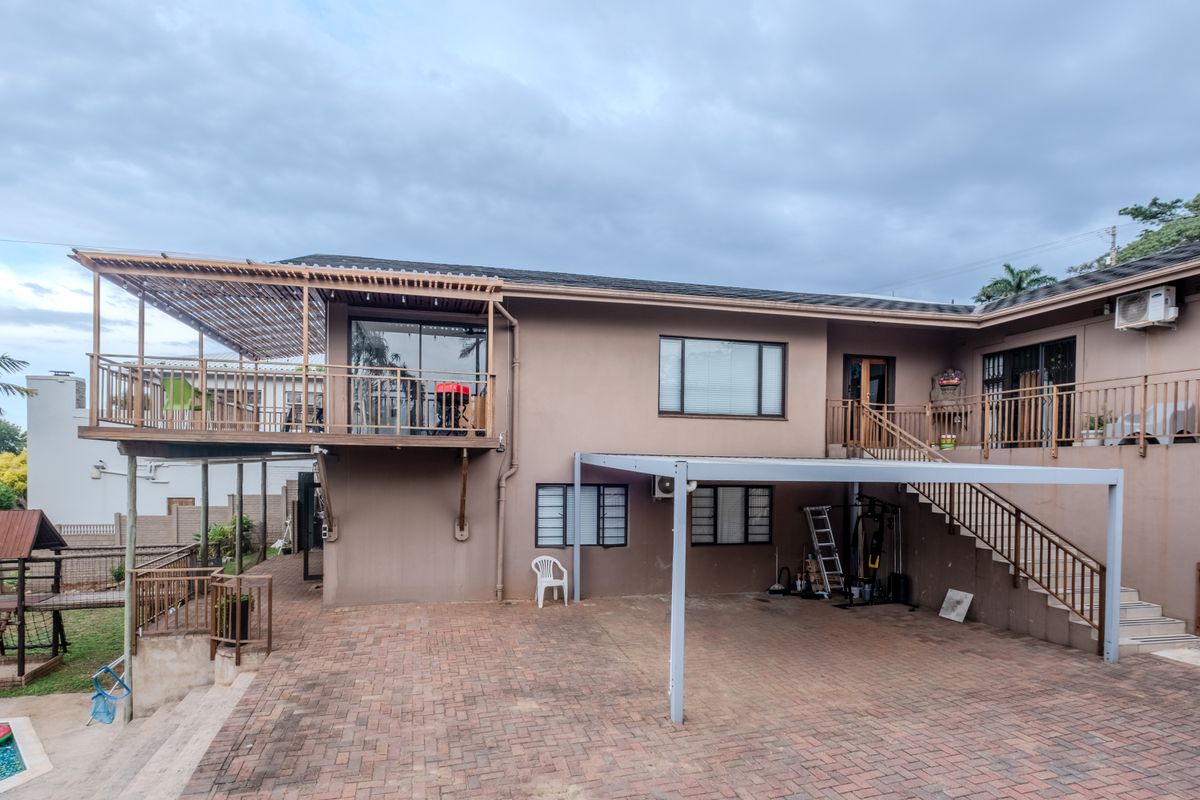 Rear exterior view featuring a raised wooden deck, paved patio area, metal staircase, and access to the garden and pool area.