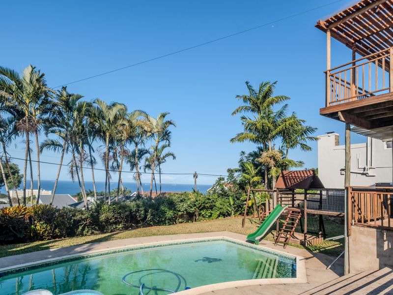 Outdoor pool area featuring a paved surround, wooden deck, and elevated balcony with scenic coastal views.