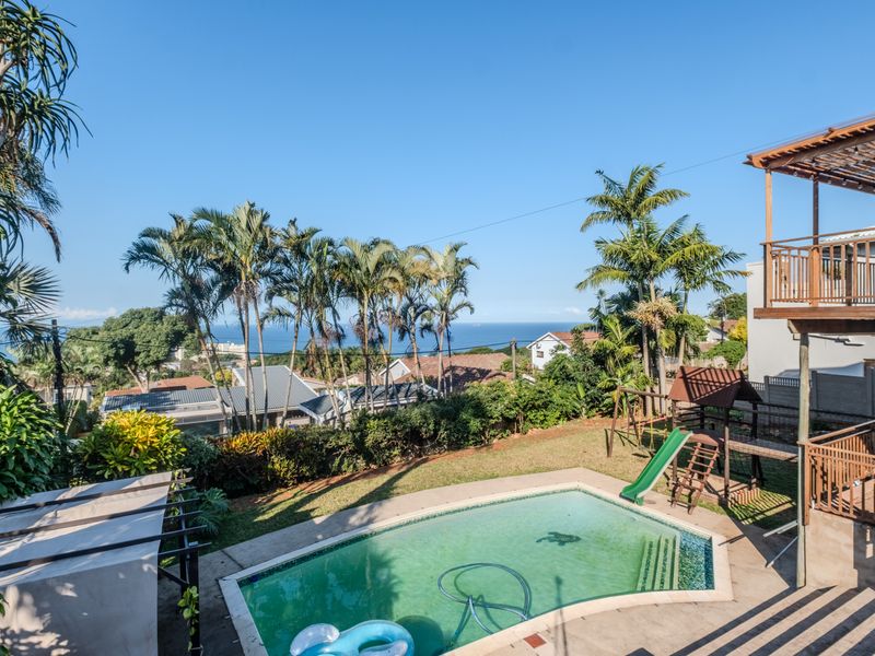 Outdoor pool area featuring a swimming pool, paved patio, and elevated wooden deck with scenic coastal views.