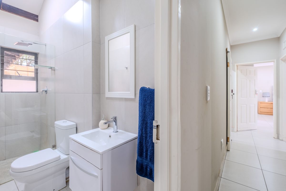 A clean, modern bathroom featuring a vanity with basin, a toilet, and a glass-enclosed shower with a rain shower head.