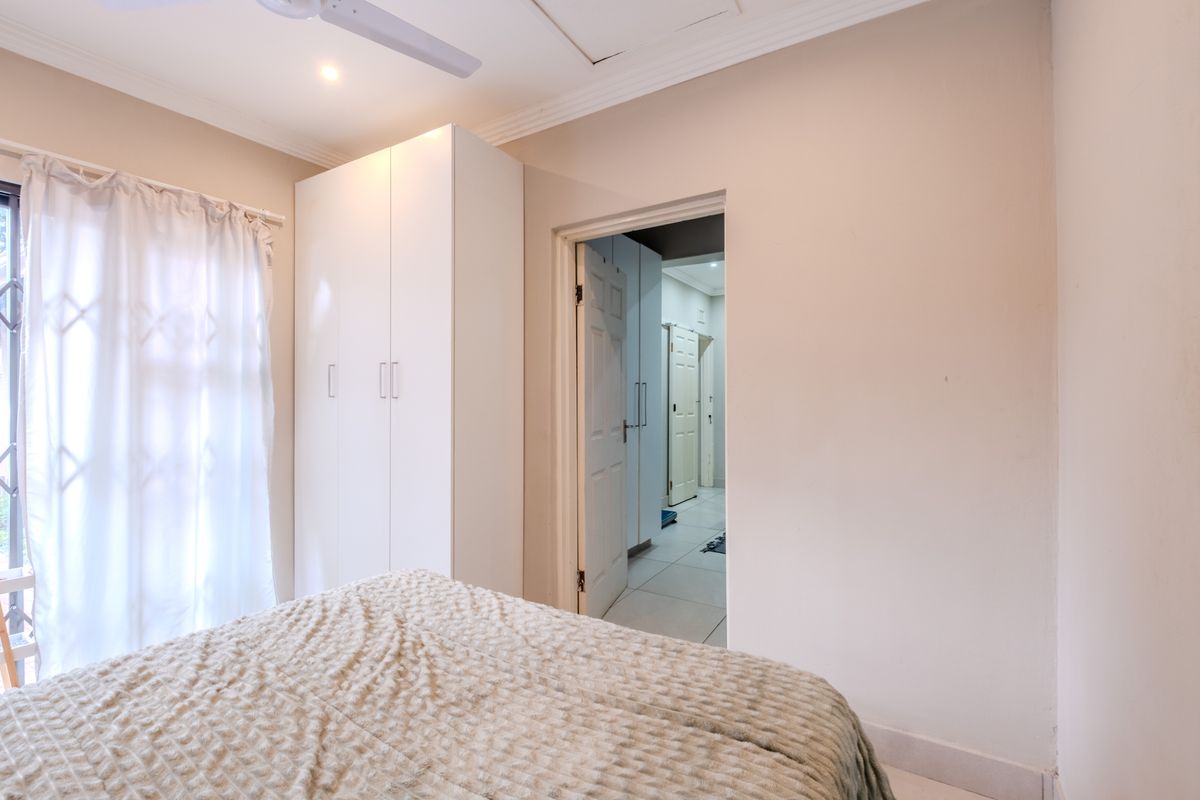 A well-maintained bedroom featuring a built-in wardrobe, ceiling fan, and neutral finishes, with a doorway leading to an adjacent hallway.