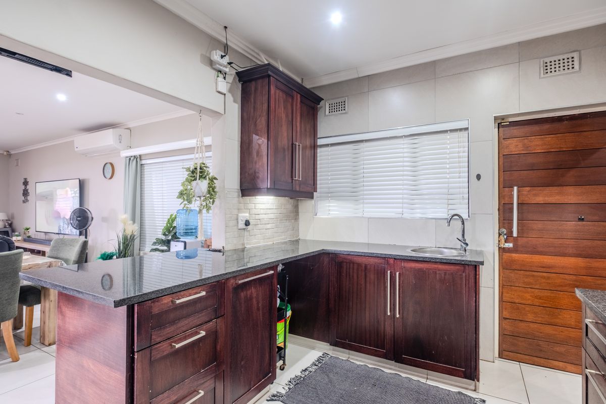 A functional kitchen featuring dark wood cabinetry, granite countertops, and a tiled backsplash, seamlessly connected to the adjacent living area.