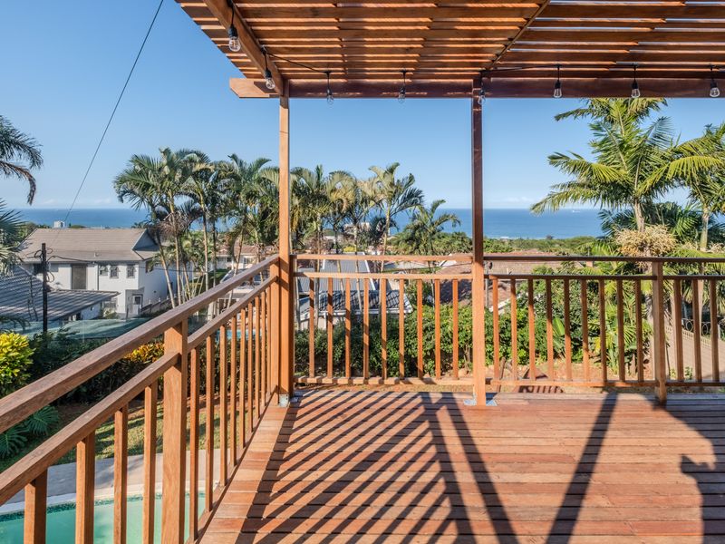 Elevated timber deck featuring a pergola and balustrade, offering expansive coastal views and overlooking the garden and pool area.