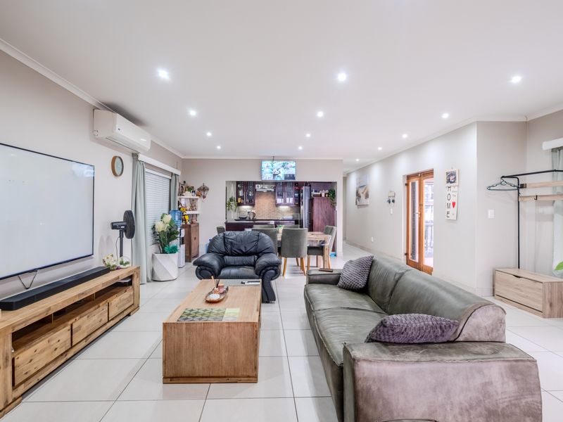 Spacious open-plan living and dining area featuring neutral tiled flooring, recessed downlighting, and a split-system air conditioner, flowing into the kitchen.