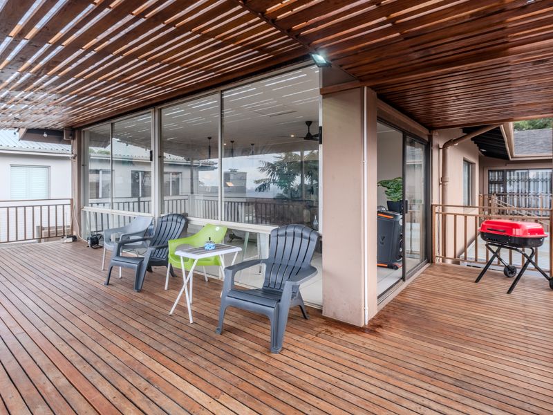 Spacious covered timber deck featuring a pergola roof, metal balustrades, and large sliding glass doors providing seamless indoor-outdoor flow.