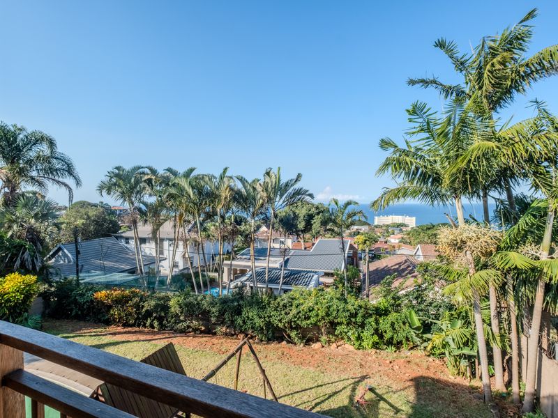 Elevated view overlooking the surrounding residential neighborhood with distant ocean vistas, framed by a wooden balcony railing.