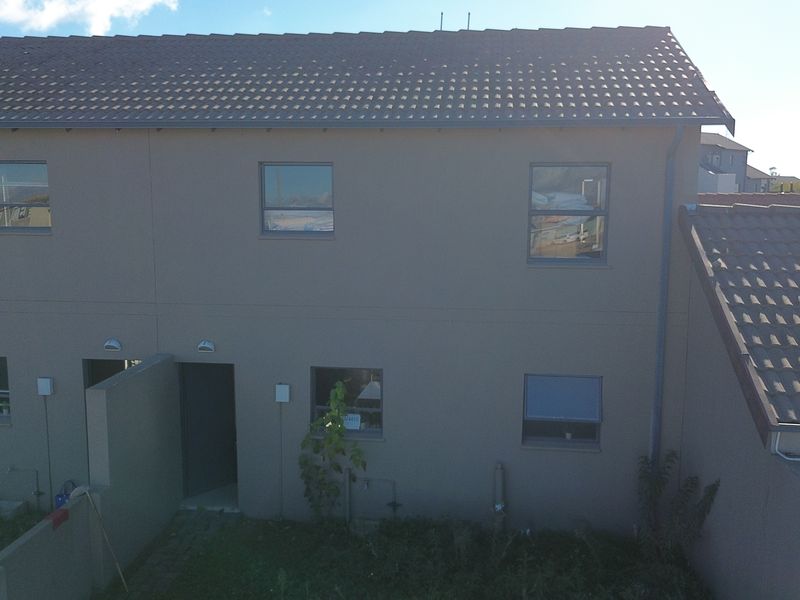 Rear elevation of a double-storey townhouse featuring plastered walls, tiled roofing, and a small private garden area.