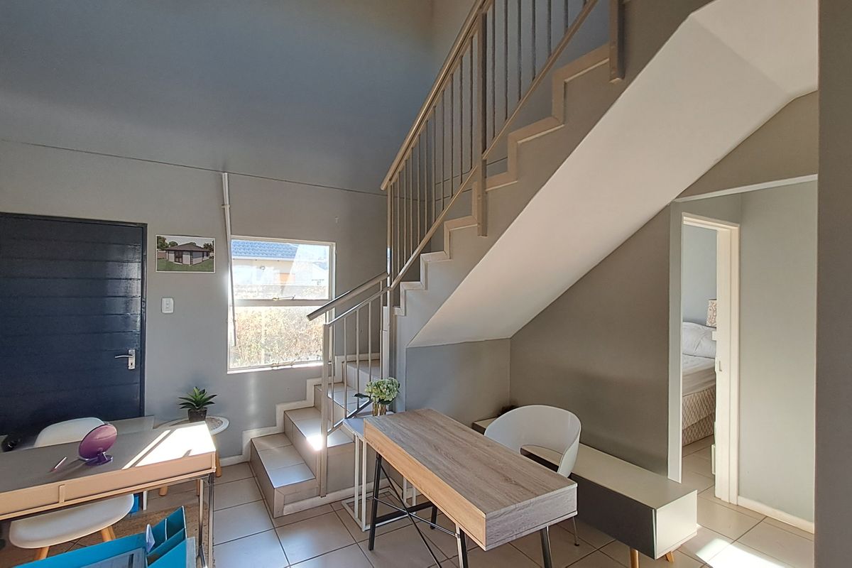 Open plan living area featuring a staircase with metal balustrade, tiled flooring, and neutral wall finishes, providing access to adjacent rooms.