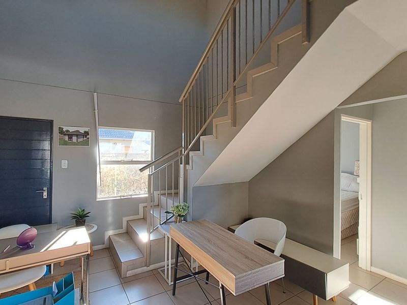 Open plan living area featuring a staircase with metal balustrade, tiled flooring, and neutral wall finishes, providing access to adjacent rooms.