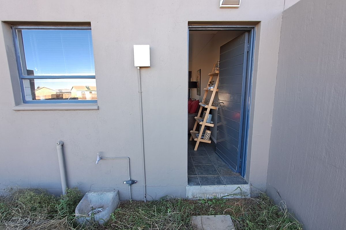 Rear exterior view of the townhouse featuring an external door, window, and utility water tap with drainage.