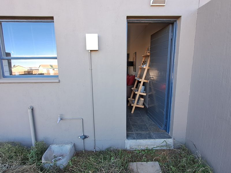 Rear exterior view of the townhouse featuring an external door, window, and utility water tap with drainage.
