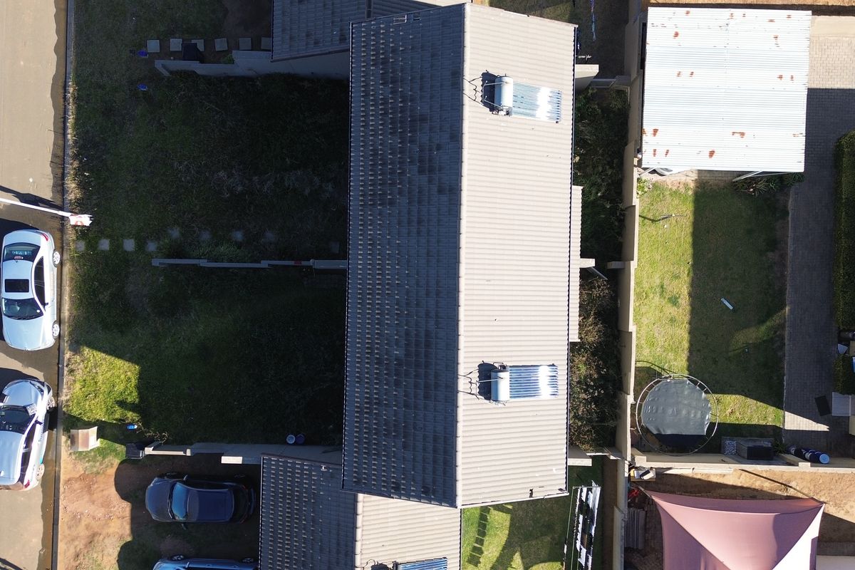 Aerial view of a townhouse property featuring a tiled roof with solar water heating systems, boundary walls, and surrounding garden space.