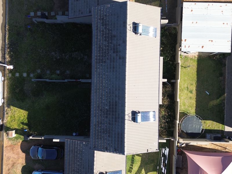 Aerial view of a townhouse property featuring a tiled roof with solar water heating systems, boundary walls, and surrounding garden space.