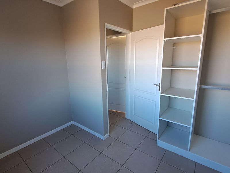A clean, empty bedroom featuring neutral wall tones, tiled flooring, and a built-in wardrobe with shelving and hanging space.