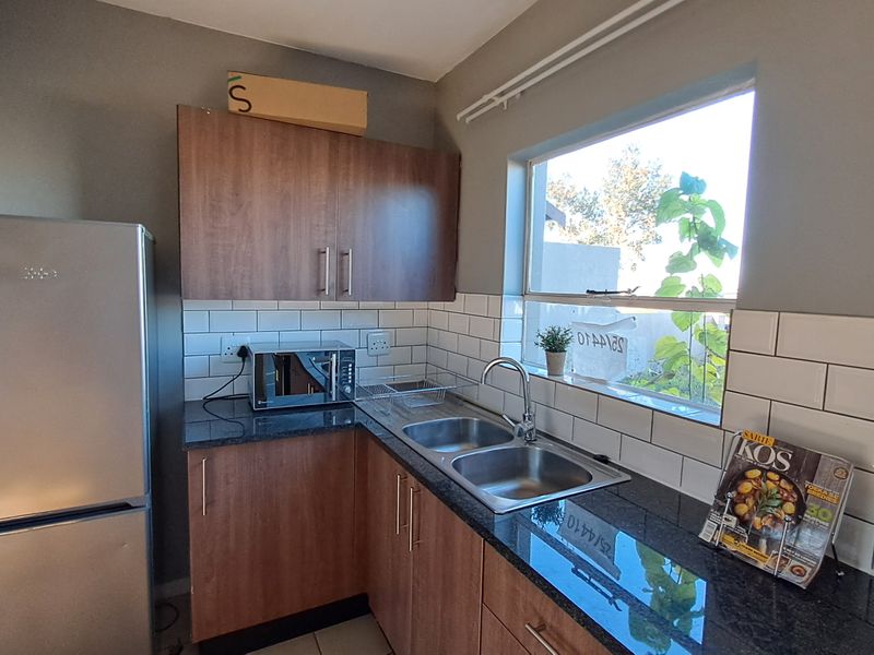 A functional kitchen featuring wood-finish cabinetry, granite countertops, a double stainless steel sink, and a classic white subway tile backsplash.