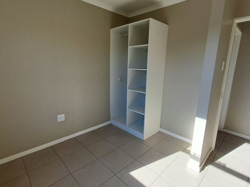 A clean, empty bedroom featuring neutral wall tones, tiled flooring, and a built-in white shelving unit for storage.