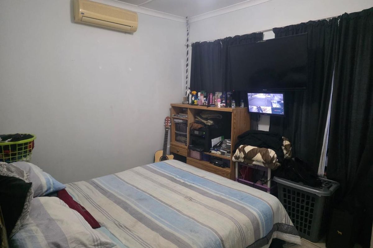 A bedroom featuring a wall-mounted air conditioning unit, tiled flooring, and window treatments.