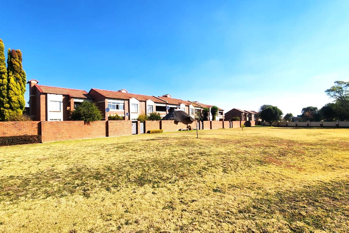 A wide-angle view of the rear exterior of the apartment complex, featuring a large communal lawn area and brick boundary walls.