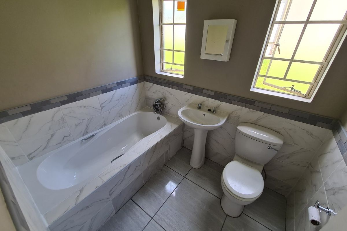 A clean, functional bathroom featuring a built-in bathtub, pedestal basin, and toilet, finished with modern marble-look wall tiles and neutral floor tiling.