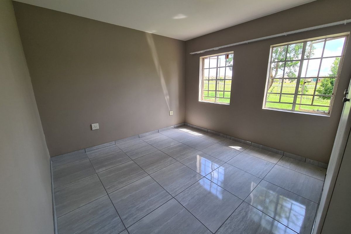 A bright, empty bedroom featuring neutral wall paint, modern grey tiled flooring, and two windows with security bars overlooking the exterior.