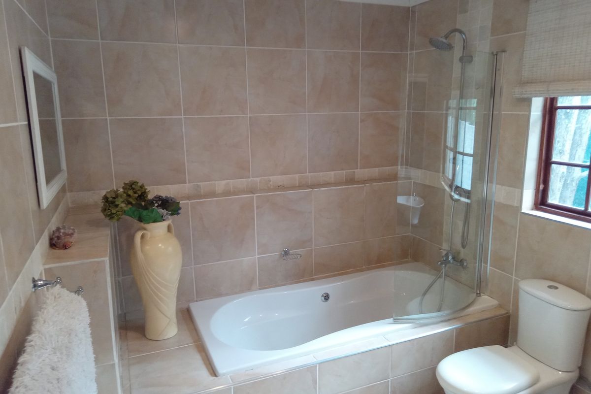 A functional bathroom featuring a built-in bathtub with a glass shower screen, wall-mounted shower head, and a standard toilet.