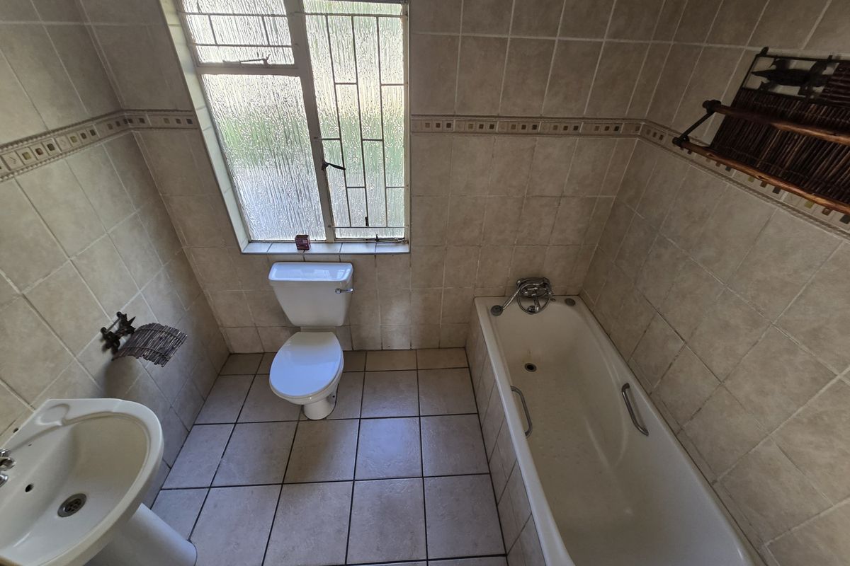 A functional bathroom featuring a pedestal basin, toilet, and bathtub with neutral wall and floor tiling.