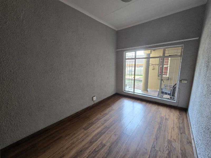 An empty bedroom featuring laminate flooring, textured walls, and a large window with security bars overlooking the exterior patio area.