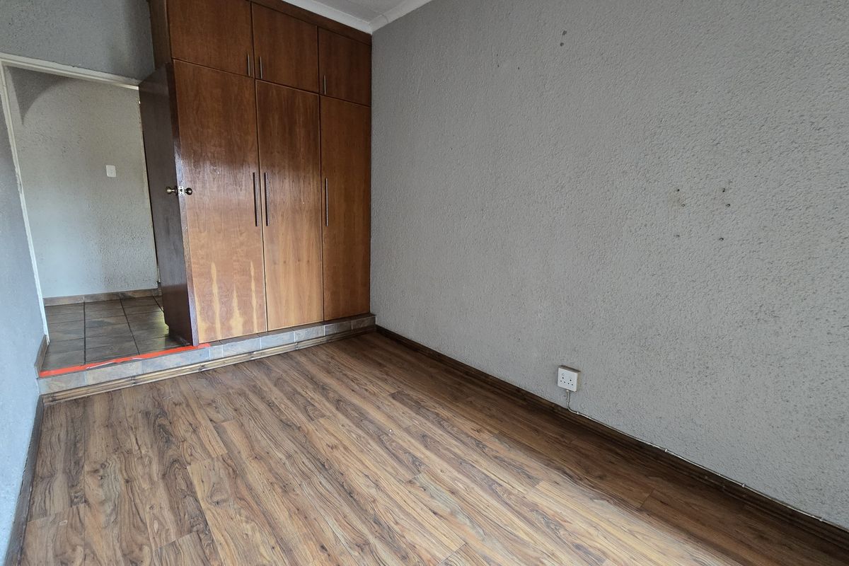 An empty bedroom featuring laminate flooring, textured walls, and built-in wooden cupboards, offering a blank canvas for renovation or interior design updates.
