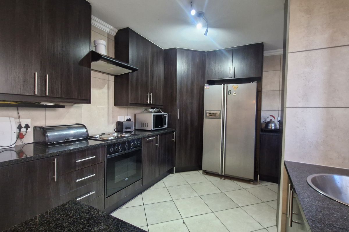 A functional kitchen featuring dark wood cabinetry, granite countertops, built-in oven with hob, extractor fan, and tiled flooring.