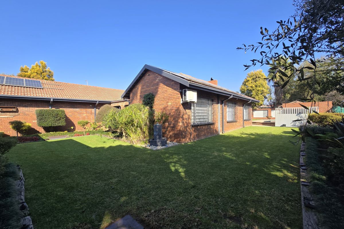 A well-maintained rear exterior view of a face brick house featuring a spacious lawn, solar panels, and secure window treatments.