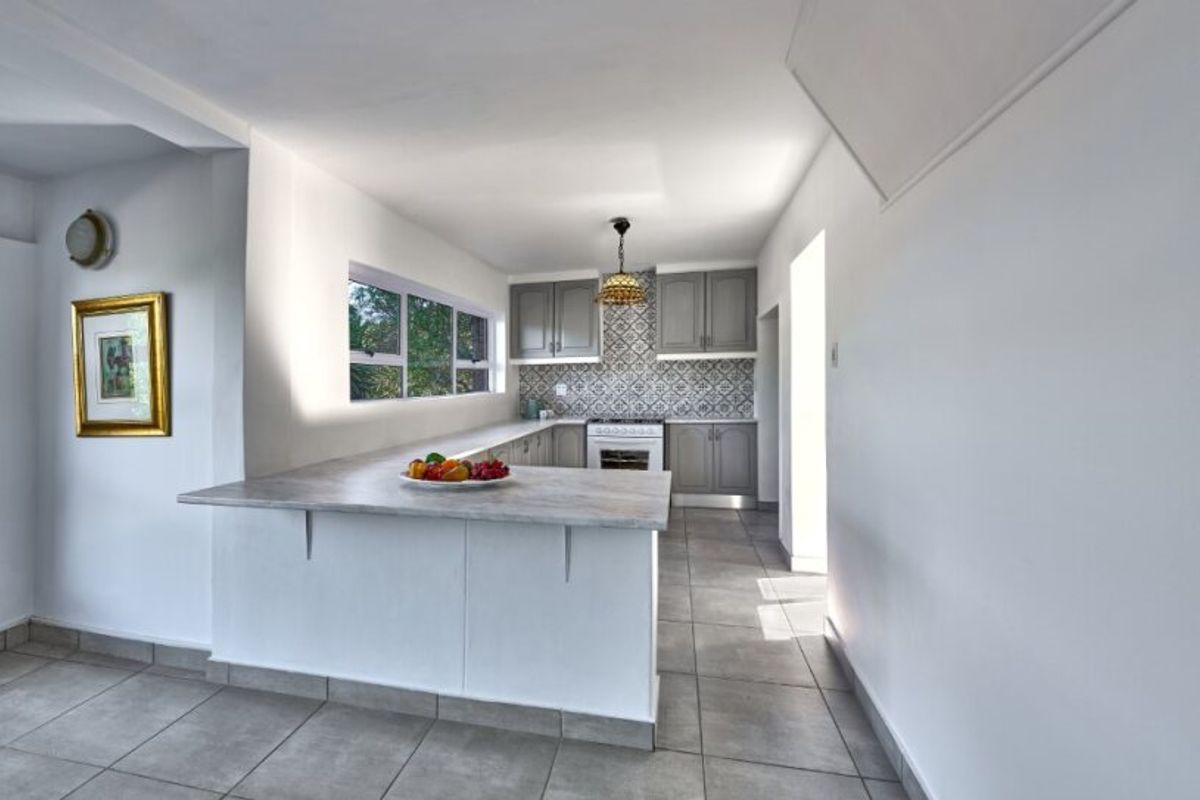 A functional kitchen featuring grey cabinetry, a patterned tile backsplash, a breakfast bar, and neutral ceramic floor tiles.