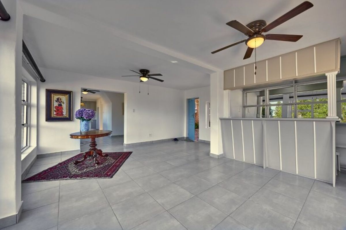 Spacious living area featuring neutral tiled flooring, dual ceiling fans, and a built-in bar counter with a pass-through window to the adjacent space.