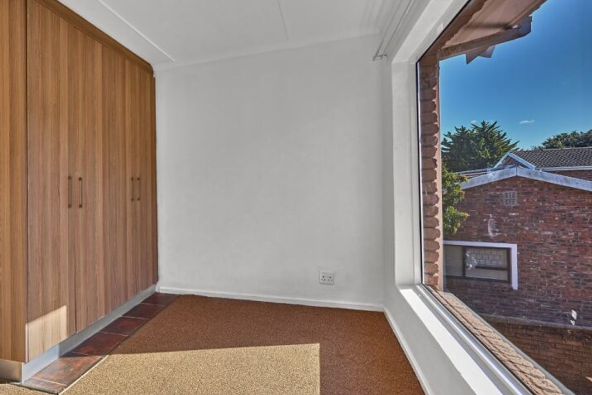 A bright, empty bedroom featuring built-in wooden cupboards, carpeted flooring, and a large window with an exterior view.