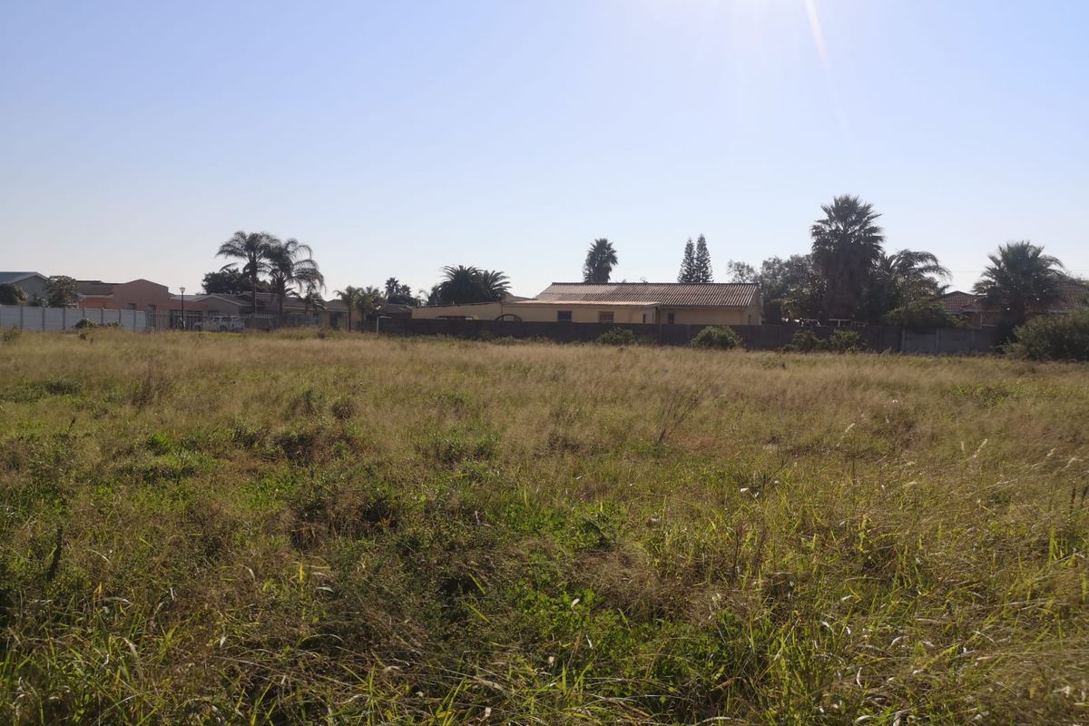 A vacant residential plot featuring open grassland with perimeter walling, offering a clear view of the surrounding neighborhood.