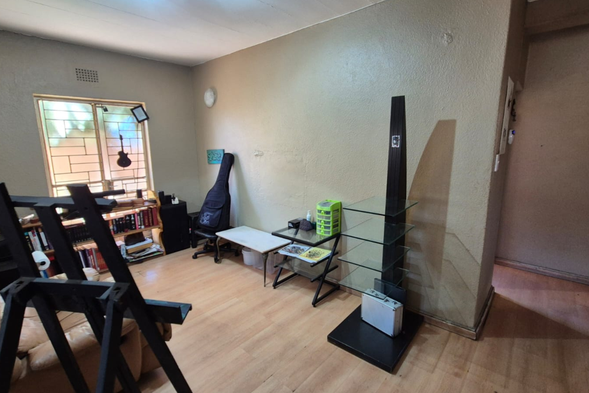 A living room area featuring laminate flooring and a window with security bars, requiring cosmetic updates to improve the overall aesthetic.