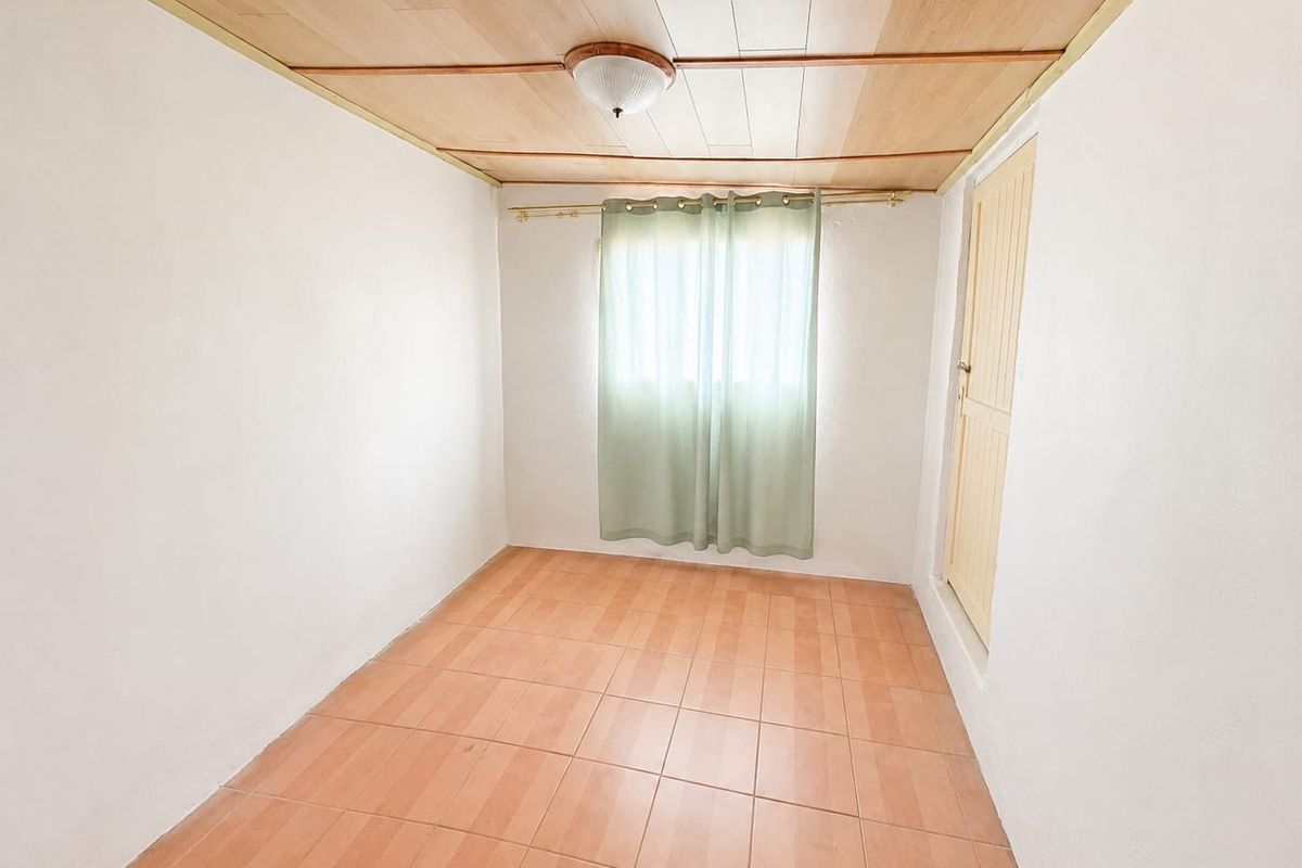 An empty bedroom featuring tiled flooring, a timber panelled ceiling, and a single timber door.
