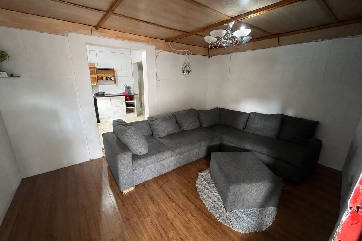 Living room featuring laminate flooring and exposed timber ceiling beams, with a direct view into the adjacent kitchen area.