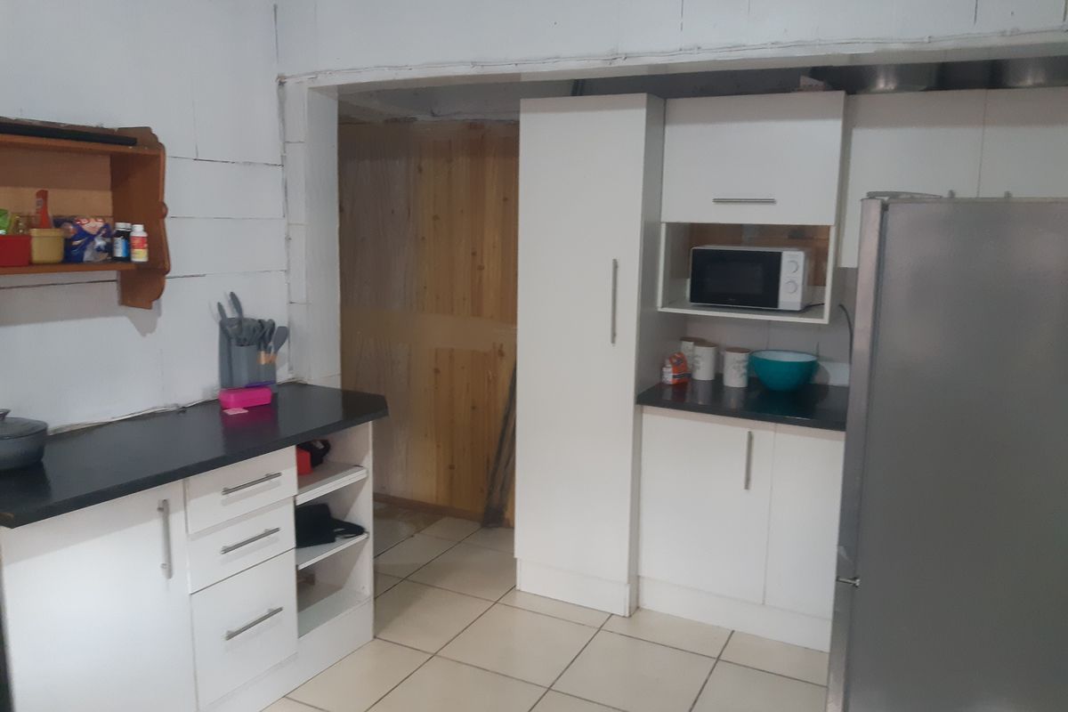 A functional kitchen area featuring white cabinetry, dark countertops, and tiled flooring, currently showing unfinished wall surfaces and structural elements.