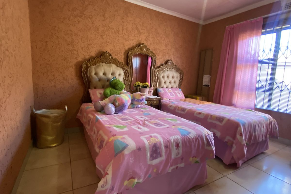 A bedroom featuring tiled flooring, textured walls, and a window fitted with security bars.