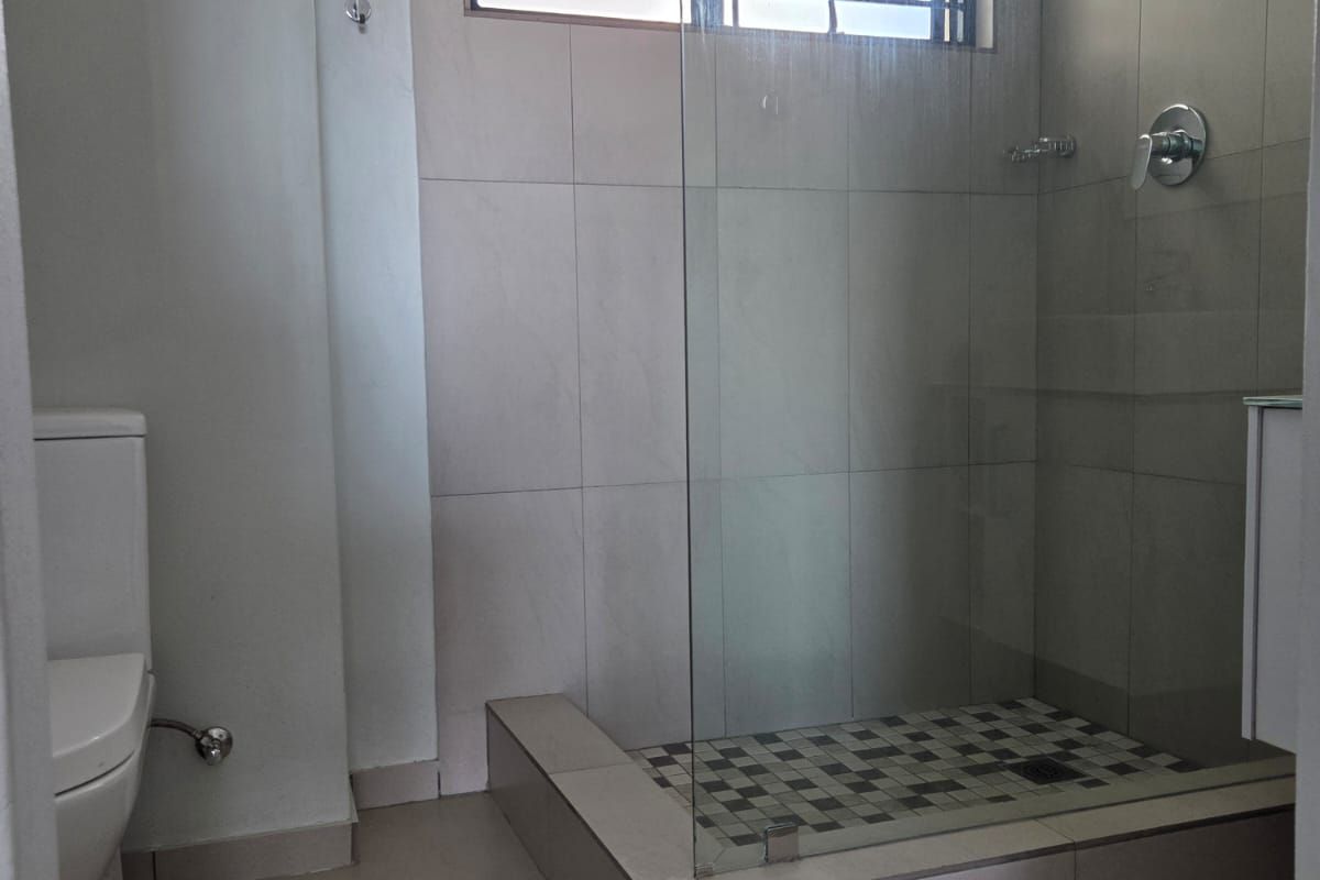 A clean, modern bathroom featuring a glass-enclosed walk-in shower with mosaic floor tiling and neutral wall tiles.