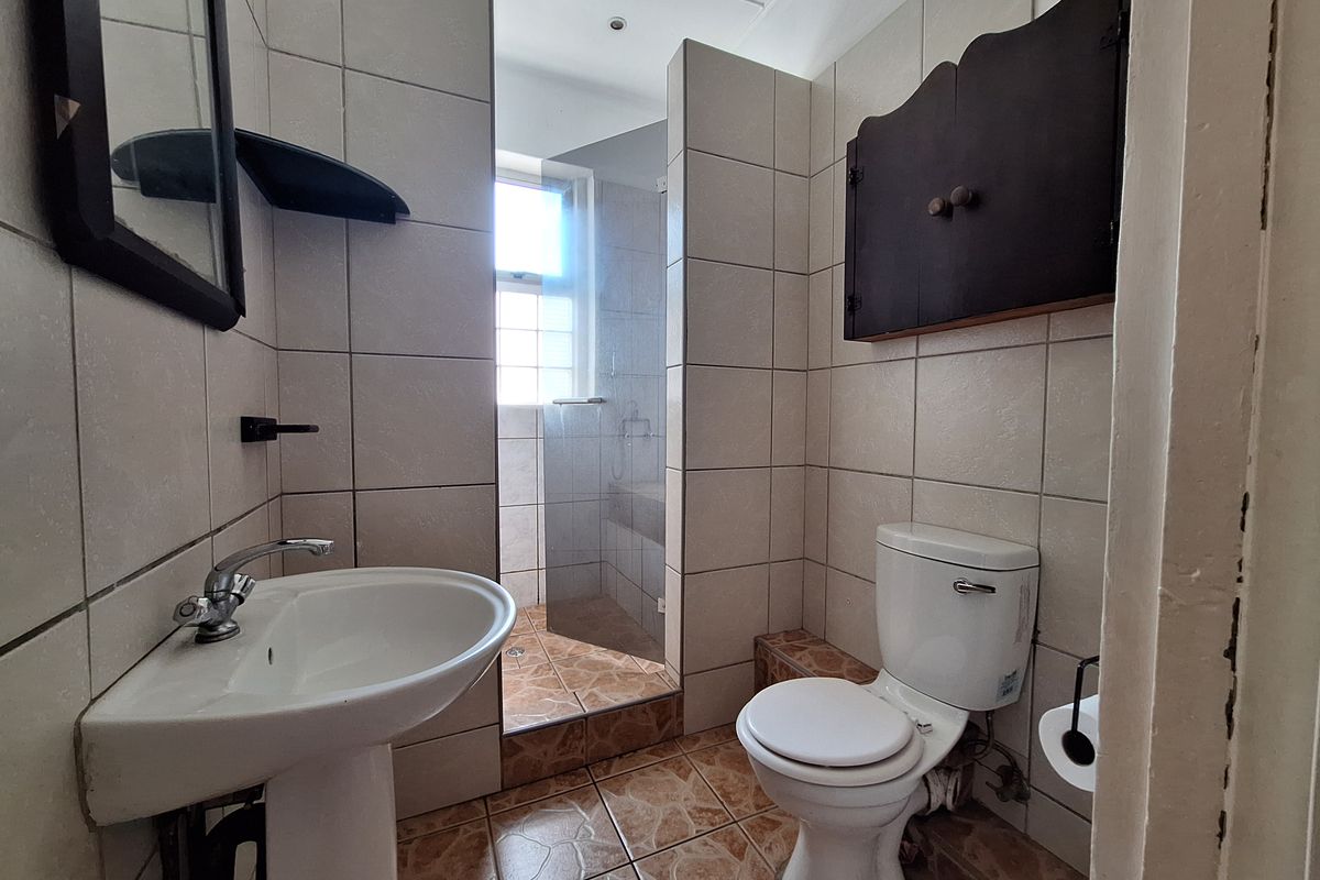 A functional bathroom featuring a pedestal washbasin, toilet, and a walk-in shower with a glass screen, finished with neutral wall and patterned floor tiles.