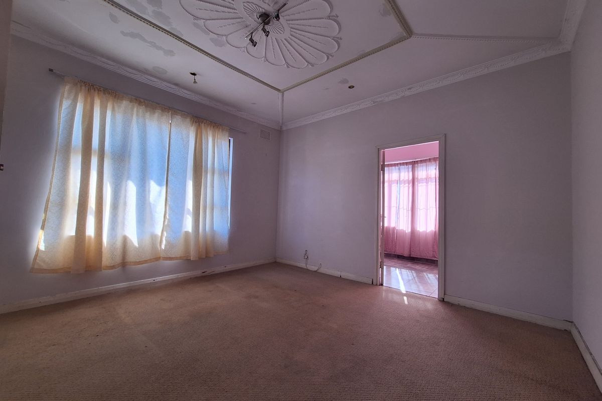 An empty living room featuring an ornate ceiling rose, decorative cornicing, and carpet flooring, requiring cosmetic updates to restore its character.