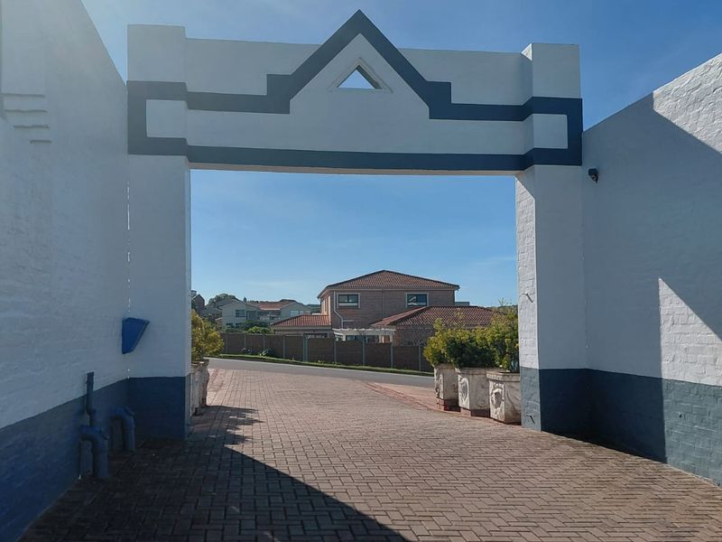 A view through a decorative painted brick archway leading to a paved driveway and residential street access.