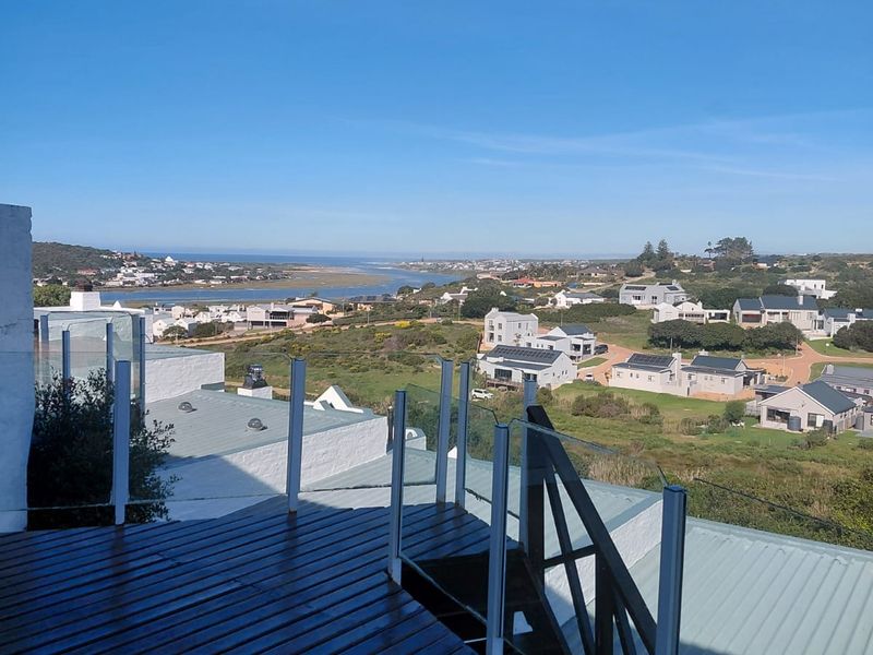 Elevated timber balcony featuring a glass balustrade and metal staircase, offering expansive coastal and landscape views.
